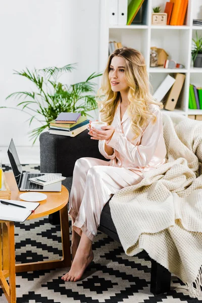 Femme détendue en pyjama assise sur le canapé et buvant du café le matin — Photo de stock