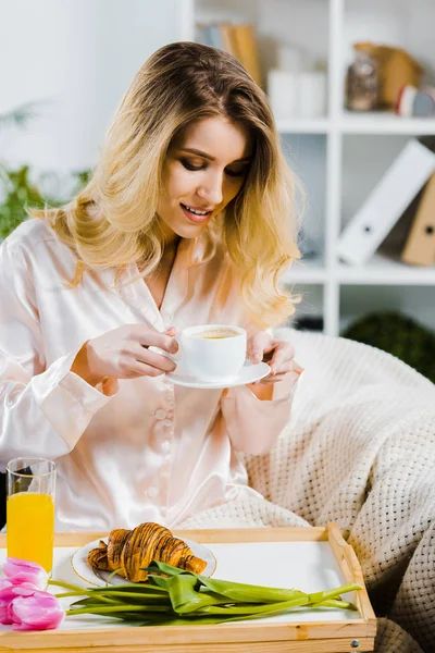 Charmante blonde Frau im Satinpyjama, die morgens Kaffee trinkt — Stockfoto