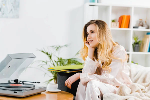 Verträumte junge Frau im Pyjama auf Sofa sitzend und Musik hörend — Stockfoto