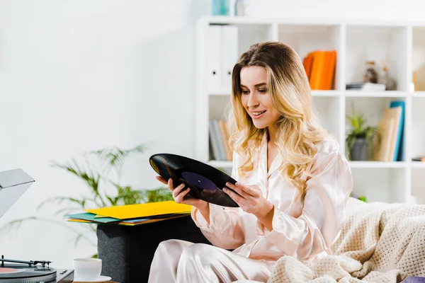 Laughing curly woman in pyjamas holding vinyl record in morning — Stock Photo