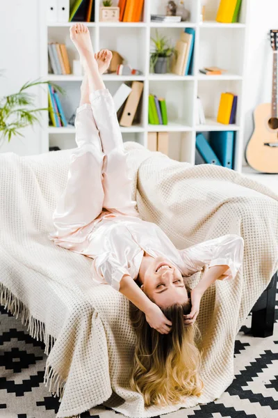 Laughing blonde woman in pyjamas lying on sofa with closed eyes — Stock Photo