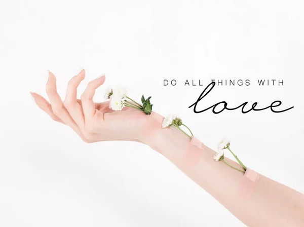 Cropped view of woman with wildflowers on hand on white background with do all things with love illustration — Stock Photo