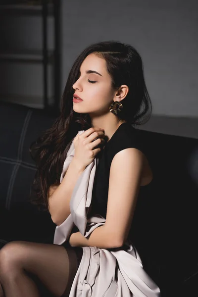 Attractive brunette woman in black elegance dress sitting with closed eyes on dark background — Stock Photo