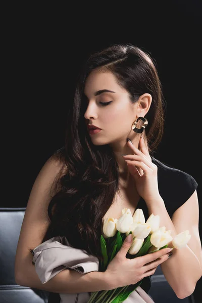 Attractive brunette woman in dress sitting with bouquet of tulips on black background — Stock Photo