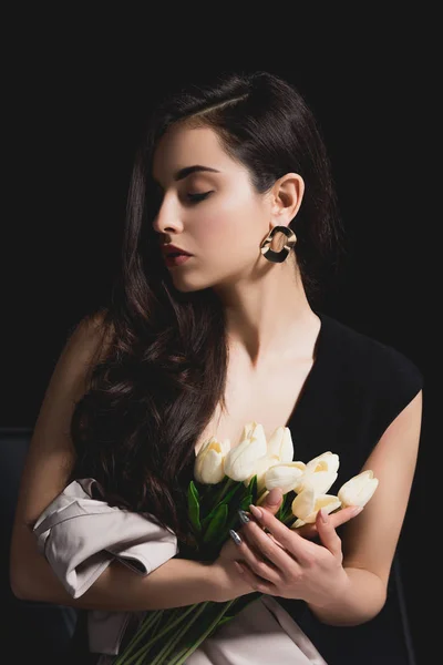 Woman in elegant dress sitting and holding bouquet with tulips on black background — Stock Photo