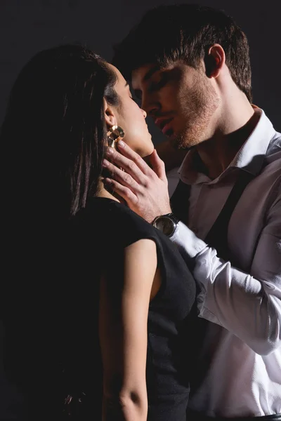 Hombre en camisa blanca y mujer en vestido negro besándose sobre fondo negro - foto de stock