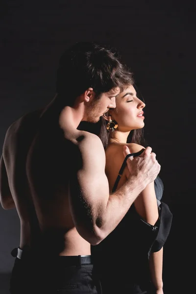 Hemdloser Mann steht und zieht attraktive brünette Frau auf schwarzem Hintergrund aus — Stockfoto