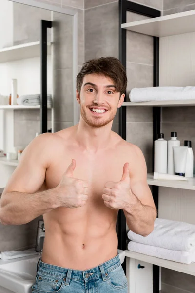 Bel homme torse nu montrant les pouces vers le haut avec les mains et souriant dans la salle de bain — Photo de stock