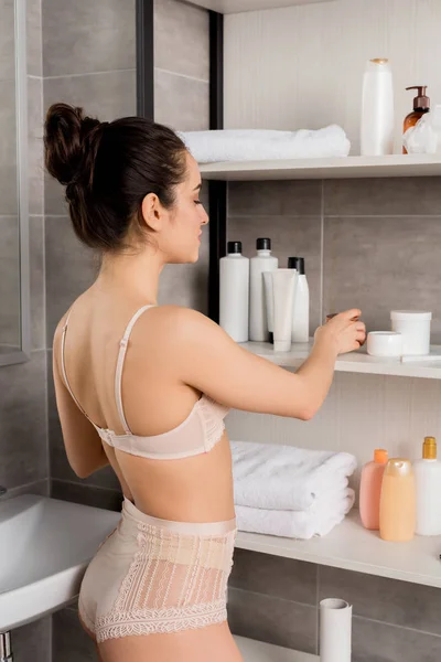 Attraktive Frau in Spitzenunterwäsche nimmt Kosmetikcreme aus dem Regal im Badezimmer — Stockfoto