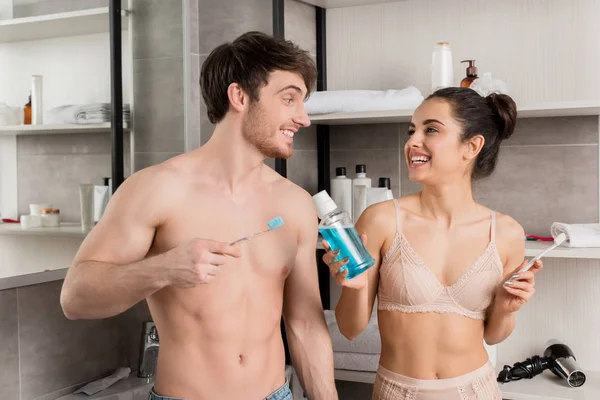 Frau mit Mundwasser in Flasche und Mann mit Zahnbürste im Badezimmer — Stockfoto