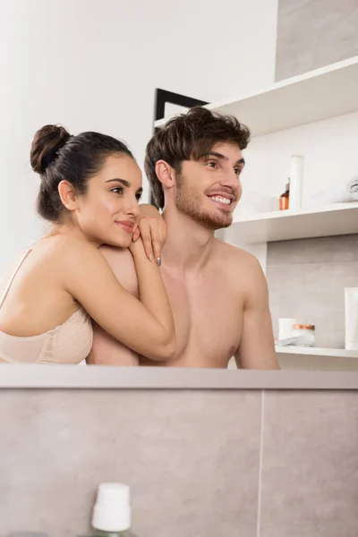 Hombre y mujer sin camisa en ropa interior de encaje abrazando y sonriendo en el baño - foto de stock