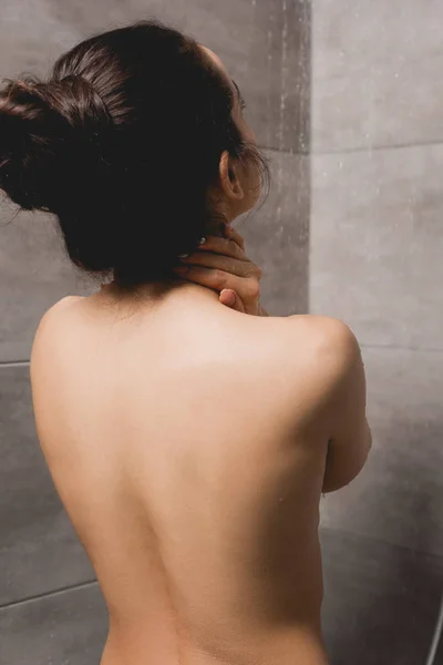 Vista trasera de mujer desnuda tomando ducha en cabina - foto de stock