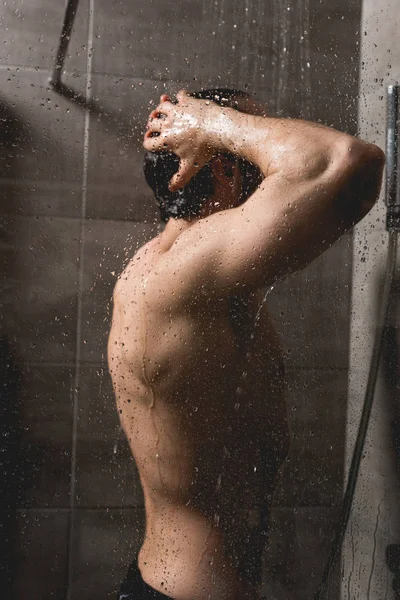 Bel homme nu prenant une douche dans la cabine — Photo de stock