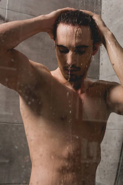 Guapo y morena hombre tomando ducha en cabina - foto de stock