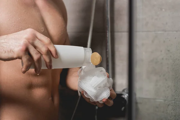 Partial view of man holding loofah and shower gel — Stock Photo