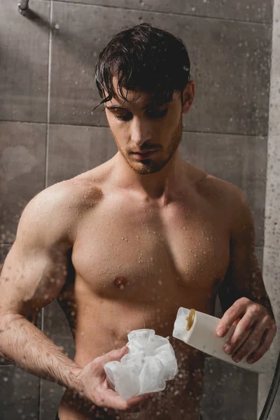 Bonito nu homem segurando loofah e chuveiro gel — Fotografia de Stock