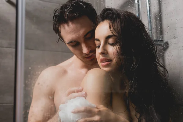 Sexy casal abraçando e tomando banho com loofah na cabine — Fotografia de Stock