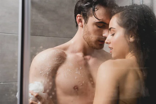 Homme et femme embrasser et prendre une douche avec loofah dans la cabine — Photo de stock