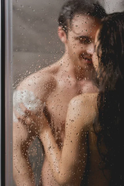 Selective focus of sexy couple hugging and taking shower with loofah in cabin — Stock Photo