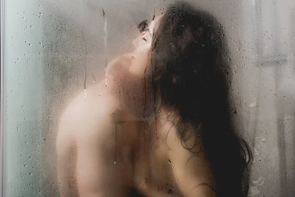 Selective focus of naked man and woman hugging and kissing in shower cabin — Stock Photo