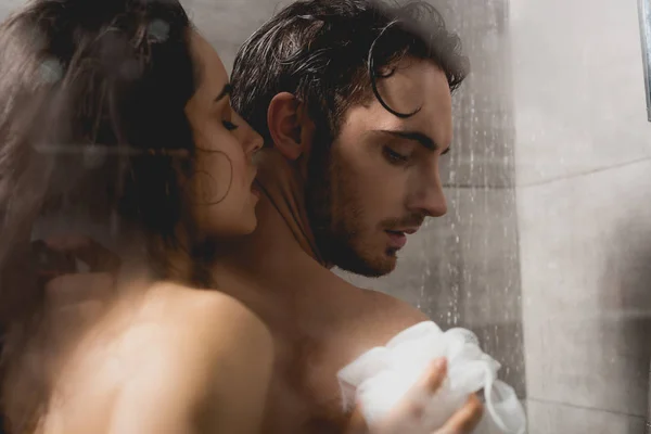 Hombre guapo y atractiva mujer abrazando y tomando ducha con esponja - foto de stock