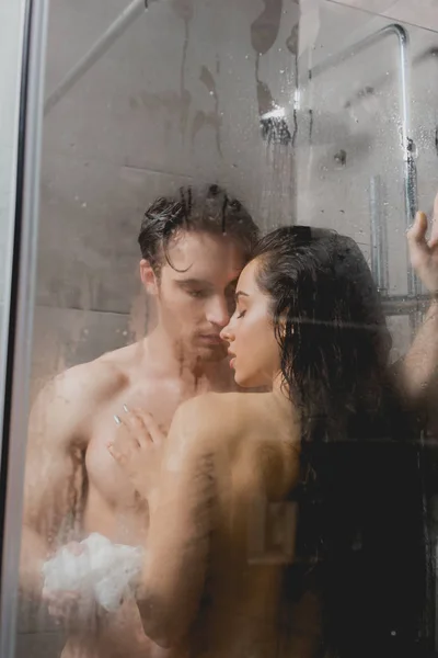 Selective focus of sexy couple hugging and taking shower with loofah — Stock Photo