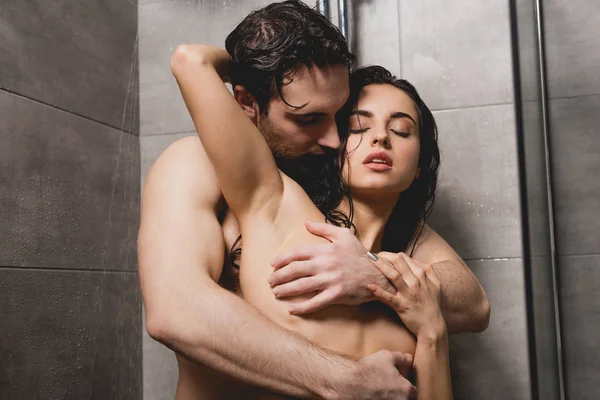 Apasionado hombre desnudo y atractiva mujer abrazándose en cabina de ducha - foto de stock