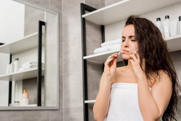 Женщина чистит зубы и разговаривает на смартфоне в ванной комнате — стоковое фото