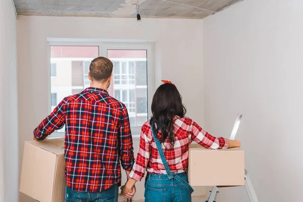 Vista trasera de pareja con cajas cogidas de la mano en casa - foto de stock