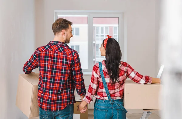 Novio y novia con cajas cogidas de la mano en casa - foto de stock