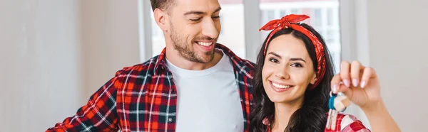 Feliz novio mirando alegre novia sosteniendo llaves en casa - foto de stock