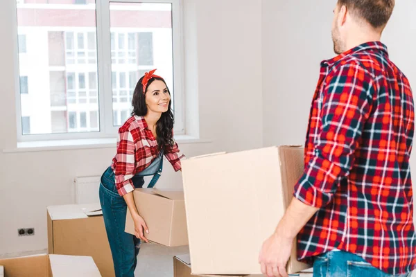Mujer feliz sosteniendo caja y mirando al hombre en casa - foto de stock