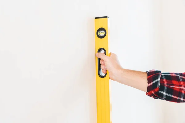 Vista cortada do homem segurando nível de medição perto da parede em casa — Fotografia de Stock