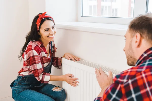 Selective fcous of happy woman touching heating radiator while looking at boyfriend at home — Stock Photo