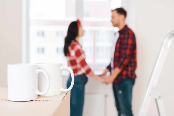 Selective focus of cups standing on box with couple holding hands on background — Stock Photo