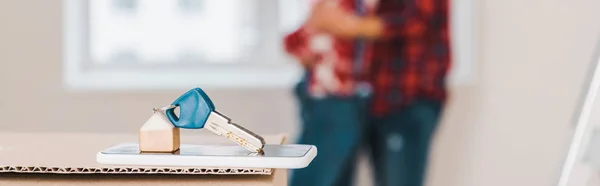 Foyer sélectif de la clé couché sur smartphone et boîte avec couple étreinte sur fond — Photo de stock