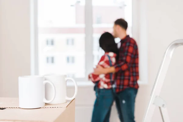 Selective focus of cups standing on box with couple hugging on background — Stock Photo