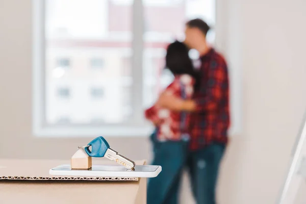 Selective focus of key lying on smartphone and box with couple hugging on background — Stock Photo