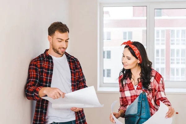 Cheerful man standing with blueprint near attractive girlfriend at home — Stock Photo
