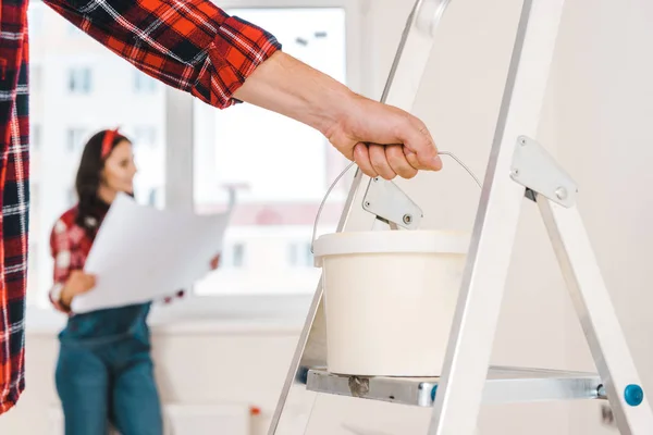 Selective focus of paint bucket in hand of man with woman holding blueprint on background — Stock Photo