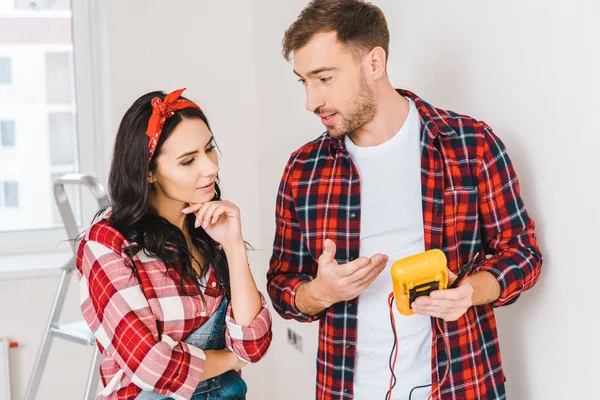 Handsome man holding digital multimeter while standing near woman at home — Stock Photo