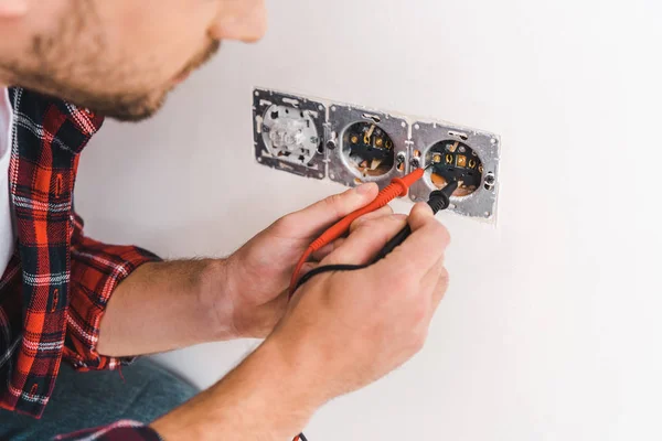 Cropped view of man holding cables near power socket at home — Stock Photo