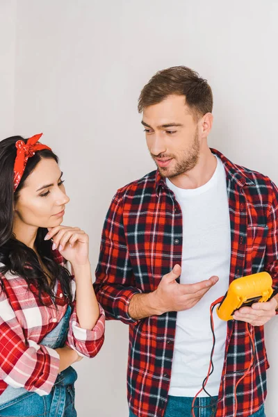 Handsome man holding digital multimeter looking at pensive woman at home — Stock Photo