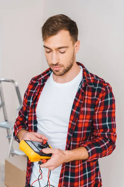 Handsome man holding digital multimeter at home — Stock Photo