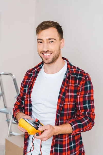 Cheerful man holding digital multimeter in hands while standing at home — Stock Photo