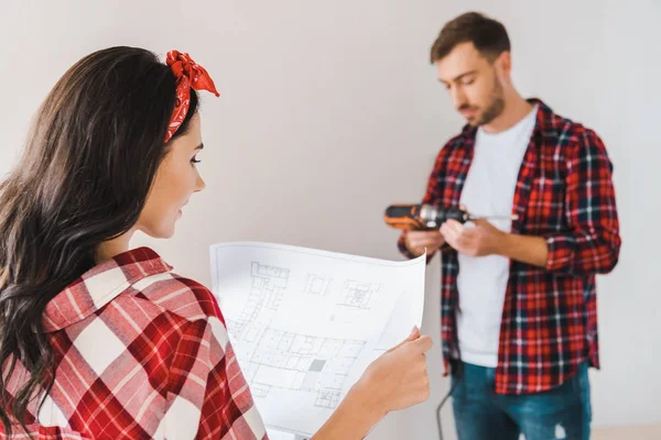 Selective focus of woman holding blueprint in hands with man on background — Stock Photo