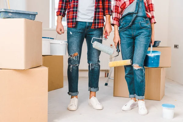 Cropped view of man and woman holding paint buckets and rollers while standing near boxes — Stock Photo