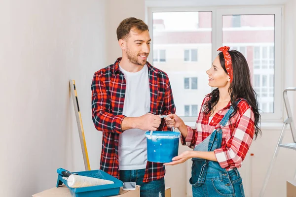 Homme tenant seau de peinture et debout près de la femme à la maison — Photo de stock