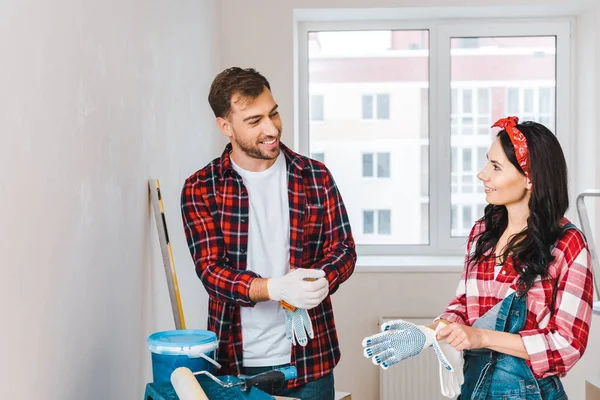 Happy man and woman wearing gloves while standing near paint bucket at home — Stock Photo