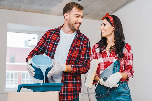 Cheerful man pouring paint bucket with blue paint near woman holding roller — Stock Photo